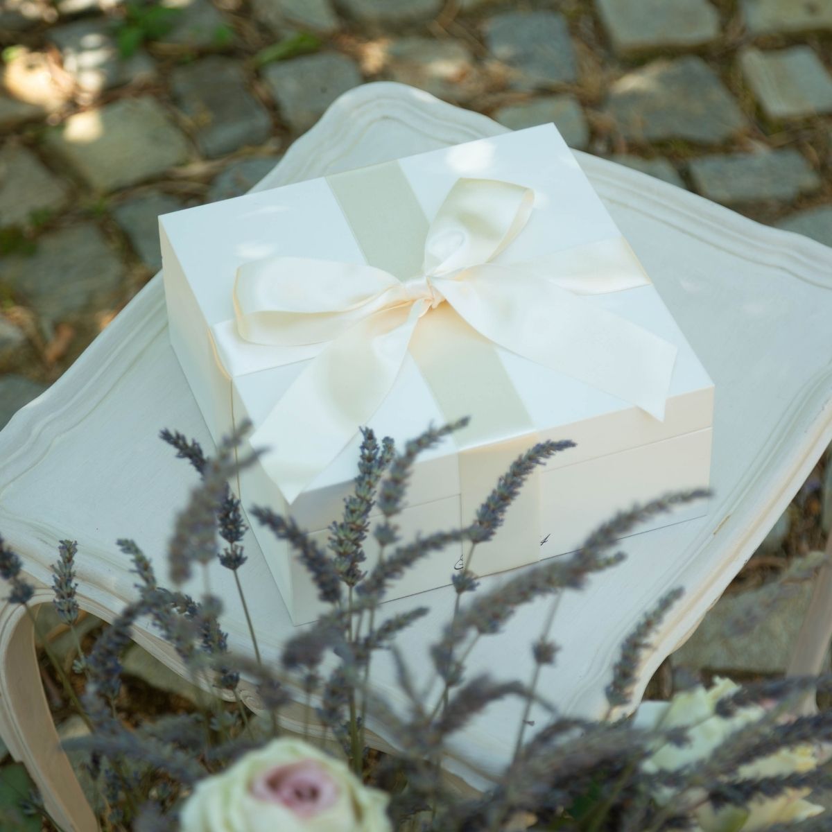 Boîte cadeau mariage luxe blanche ruban satin clair sur chaise événement. Décoration florale lavande.