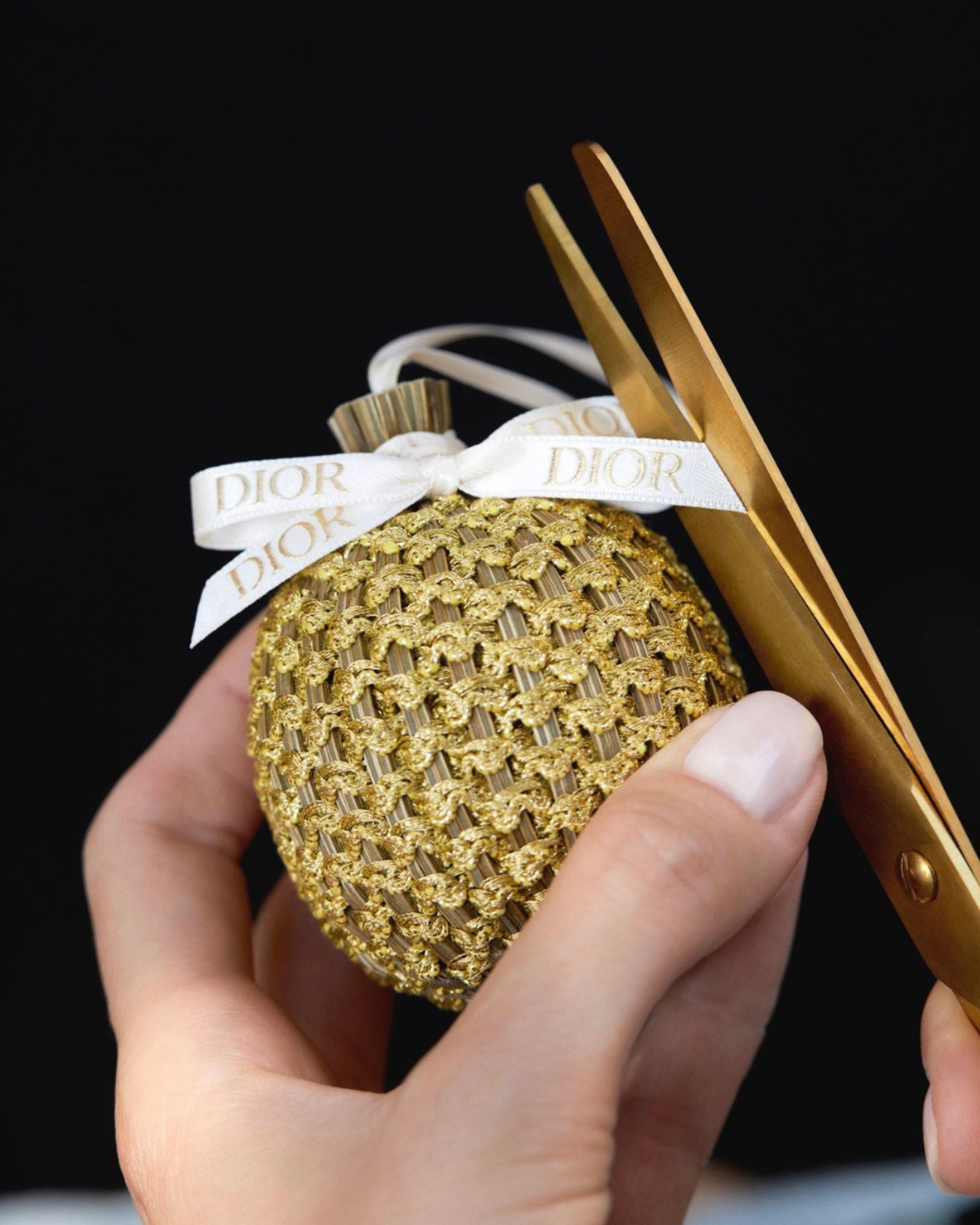 Main d'artisane en train de couper le ruban de satin Dior sur une boule de lavande vague or franc 1884 pour Dior