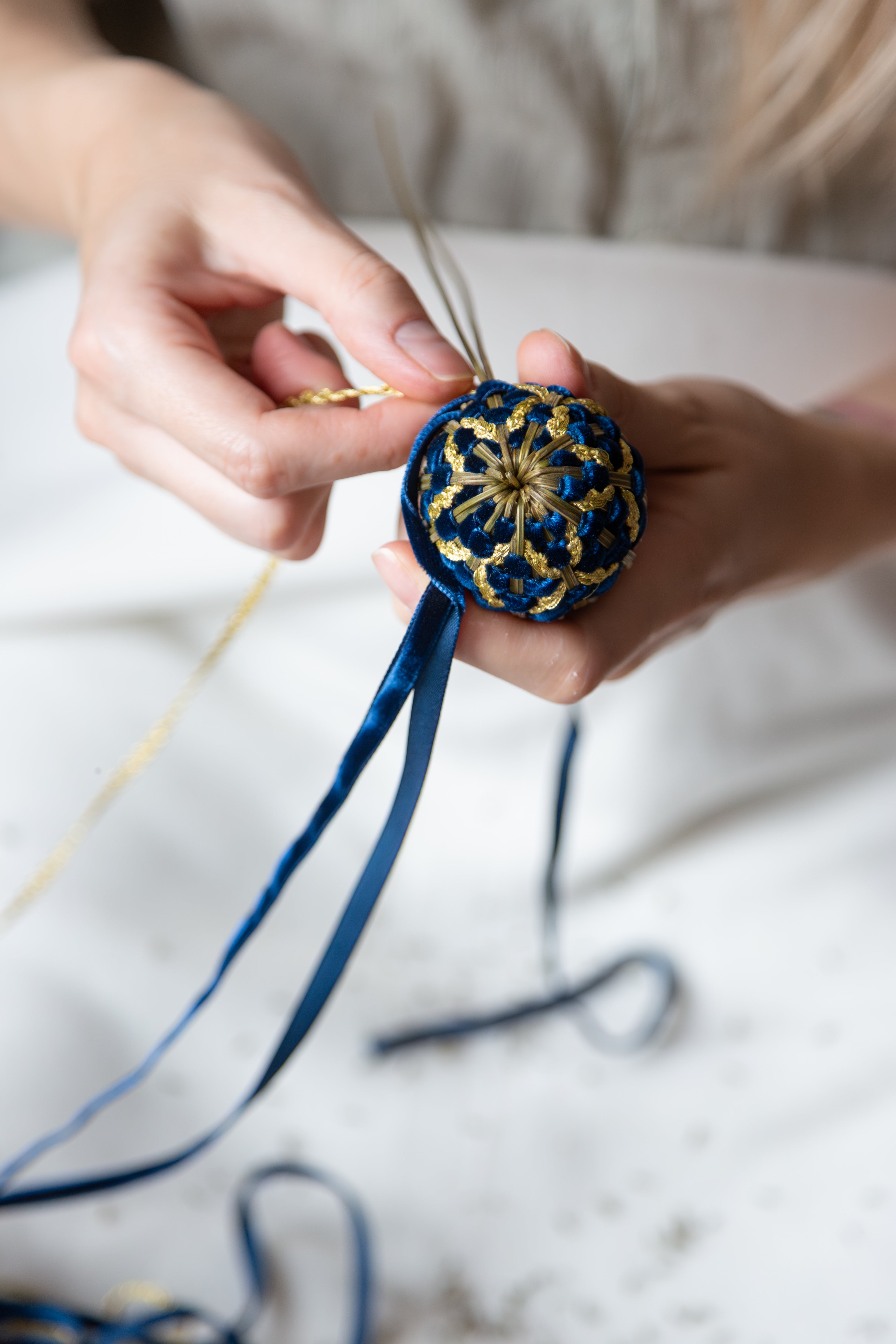 L'étape finale de la confection : les mains nouent le ruban de velours bleu sur le fuseau de lavande artisanal, symbole de la qualité française.