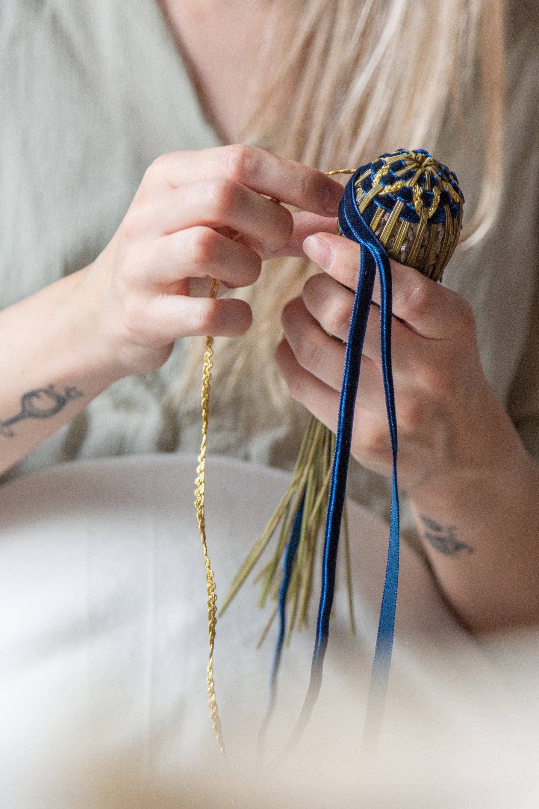 Mains d'artisane tressant un fuseau de lavande bleu et or. Illustration du savoir-faire minutieux de l'artisanat français.