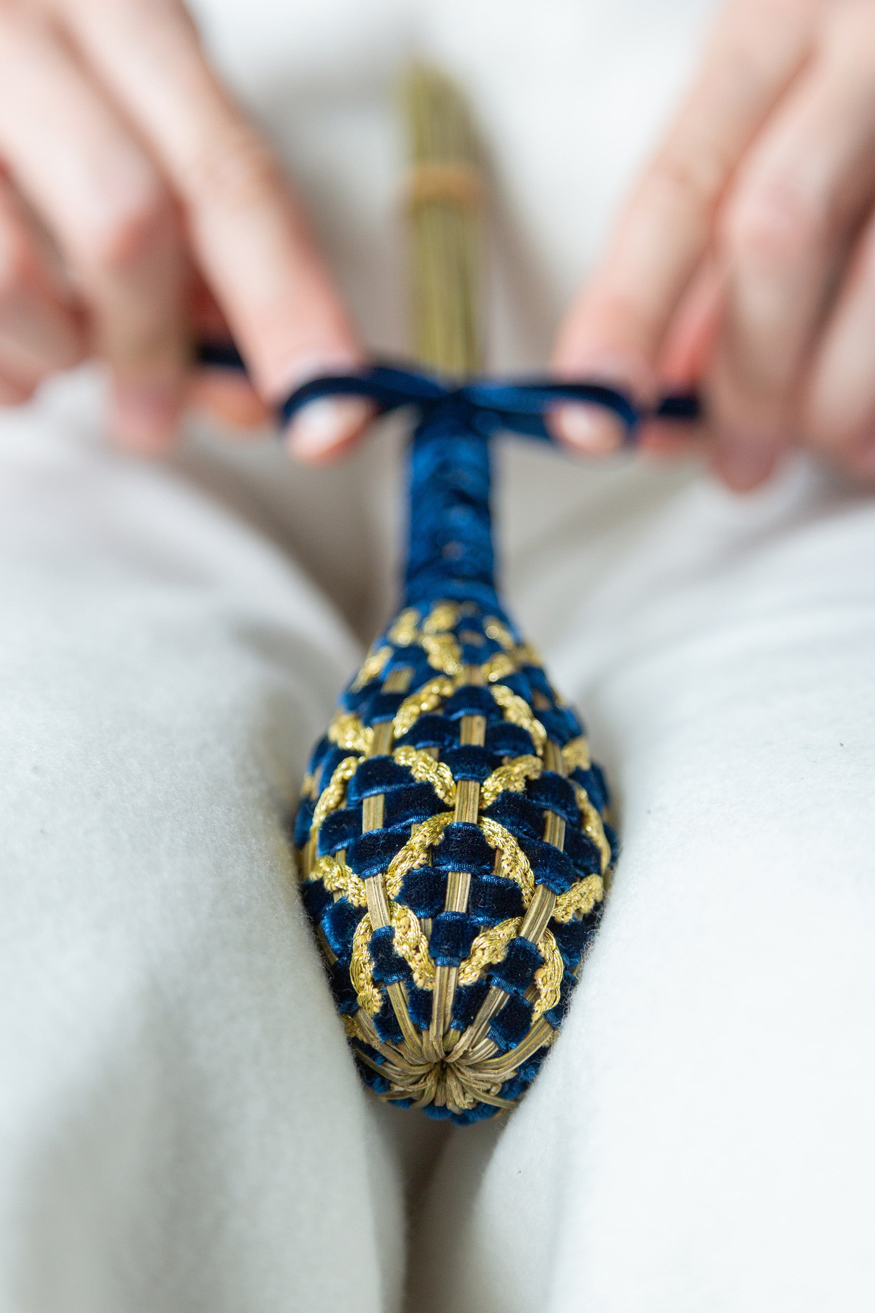 Gros plan sur le tressage du fuseau de lavande Fabergé en velours bleu marine et fil d'or, mettant en lumière la précision du geste.