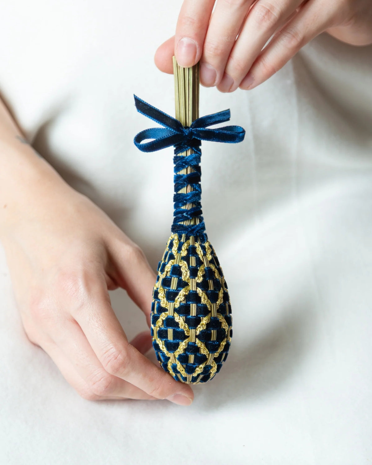 Mains tenant un fuseau de lavande tressé avec des rubans de velours bleu marine et or, noué en haut par un ruban bleu.